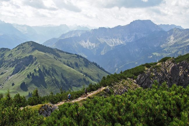 Widokowy szlak górski wiodący przez zielone połoniny z panoramą pasm górskich w tle.